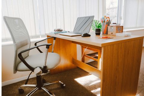 Sala com cadeira de escritório confortável e mesa para trabalho com notebook aberto e objetos em cima