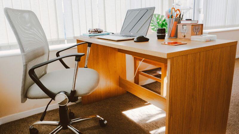 Sala com cadeira de escritório confortável e mesa para trabalho com notebook aberto e objetos em cima